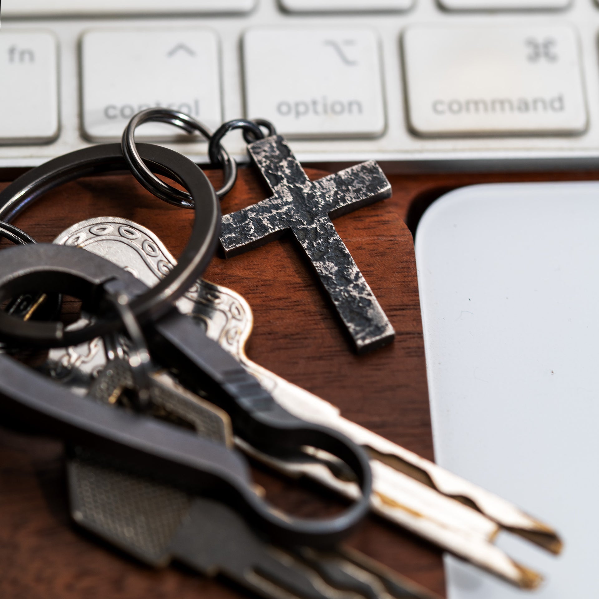Compact rock texture sterling silver cross pendant styled beside everyday keys and a laptop keyboard