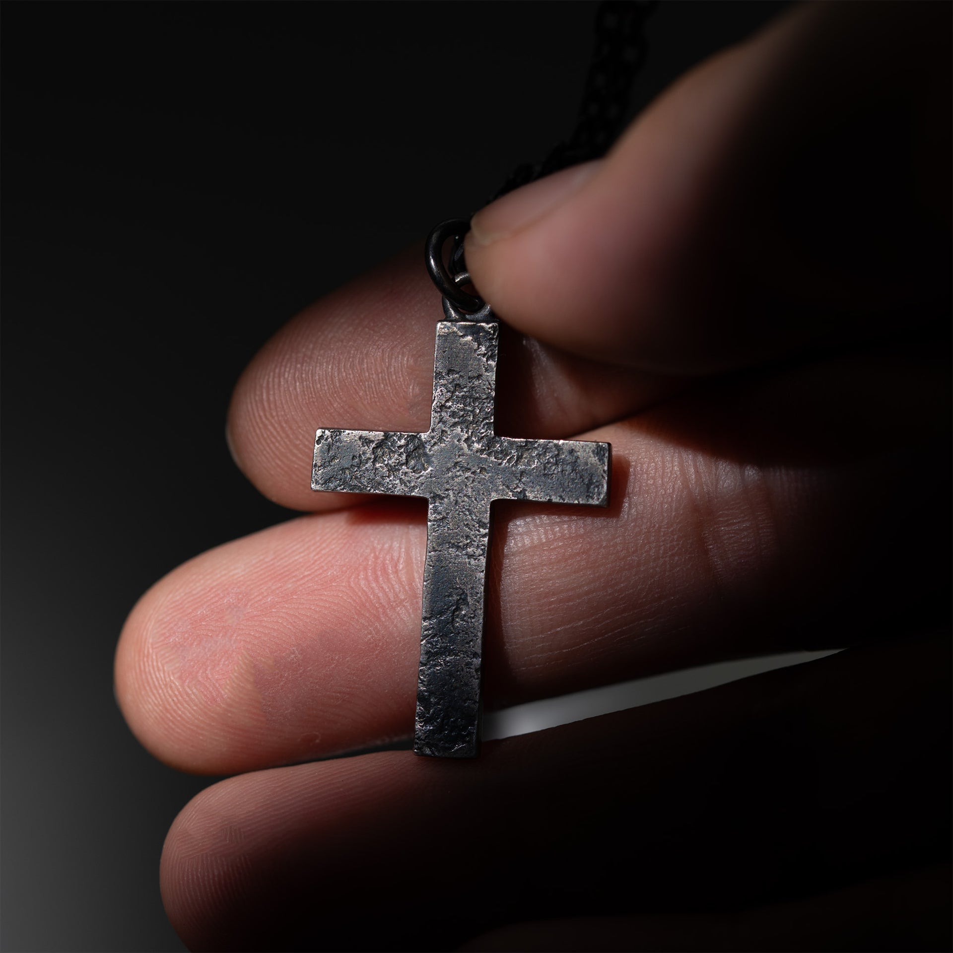 Close-up of the recessed handmade texture on a compact oxidized sterling silver cross pendant