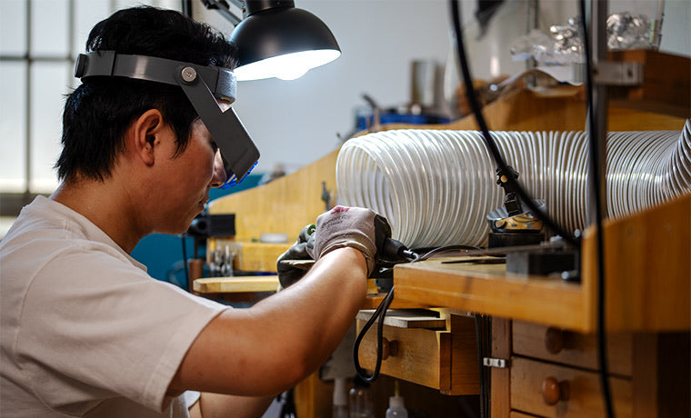 Jeweler working at the bench under magnification, hand-finishing a pendant.