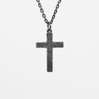 Back of the oxidized silver cross, plain with a rough carved texture and no figure or stone, hanging from a dark chain against light gray