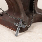 Crucifix with pink-purple cubic zirconia leaning against an old dark red metal stand, its chain draped over the stand on cream fabric