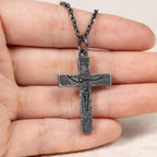 Crucifix pendant resting across the fingers of an open hand to show its size, with the purple cubic zirconia and carved figure facing up