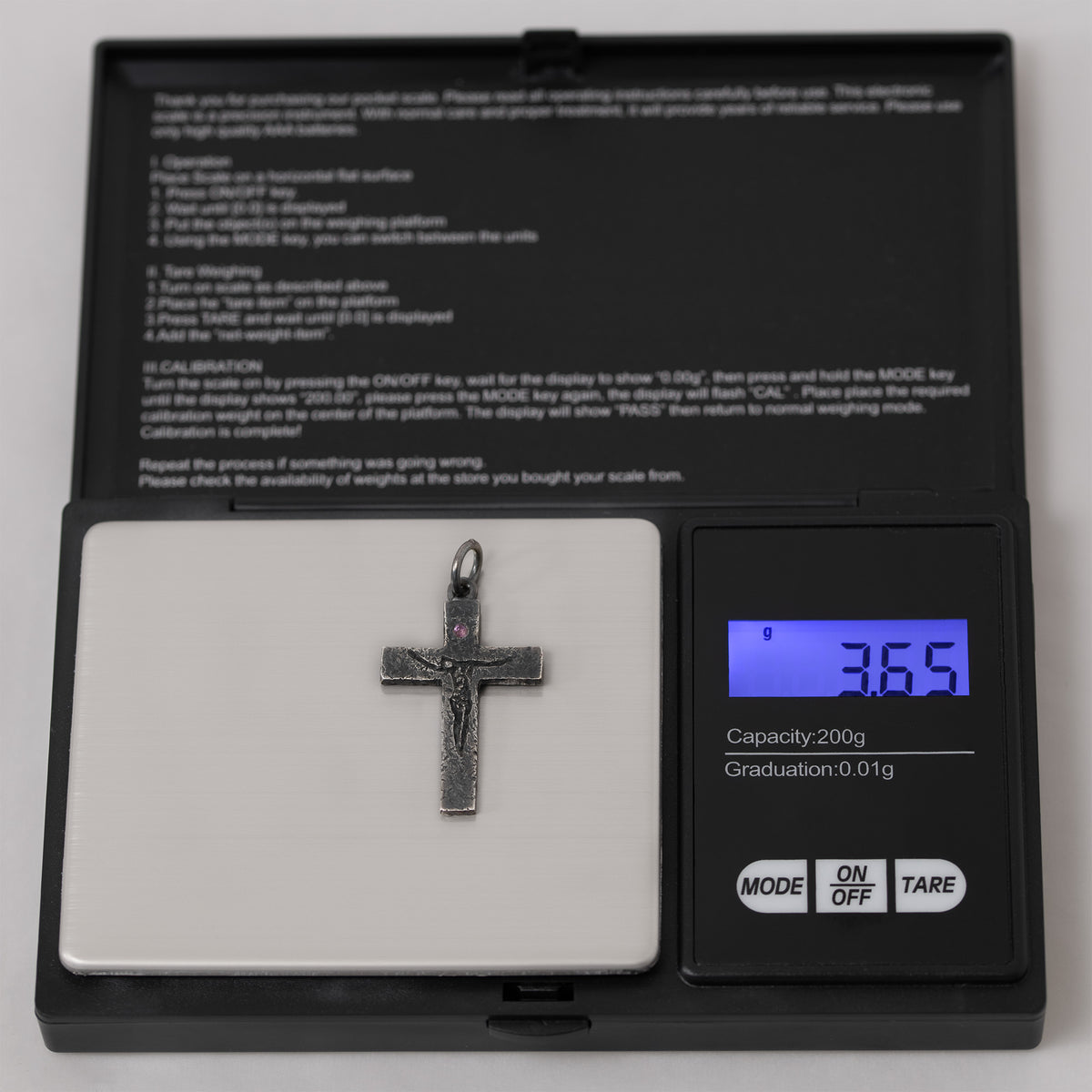 Crucifix pendant without its chain on a digital pocket scale whose display reads 3.65 g