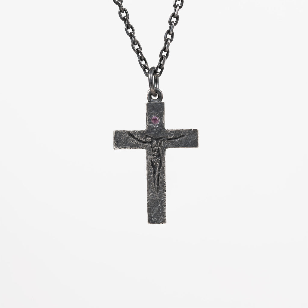 Oxidized sterling silver crucifix pendant with a small purple cubic zirconia above the carved figure of Jesus, on a dark chain against a light gray background