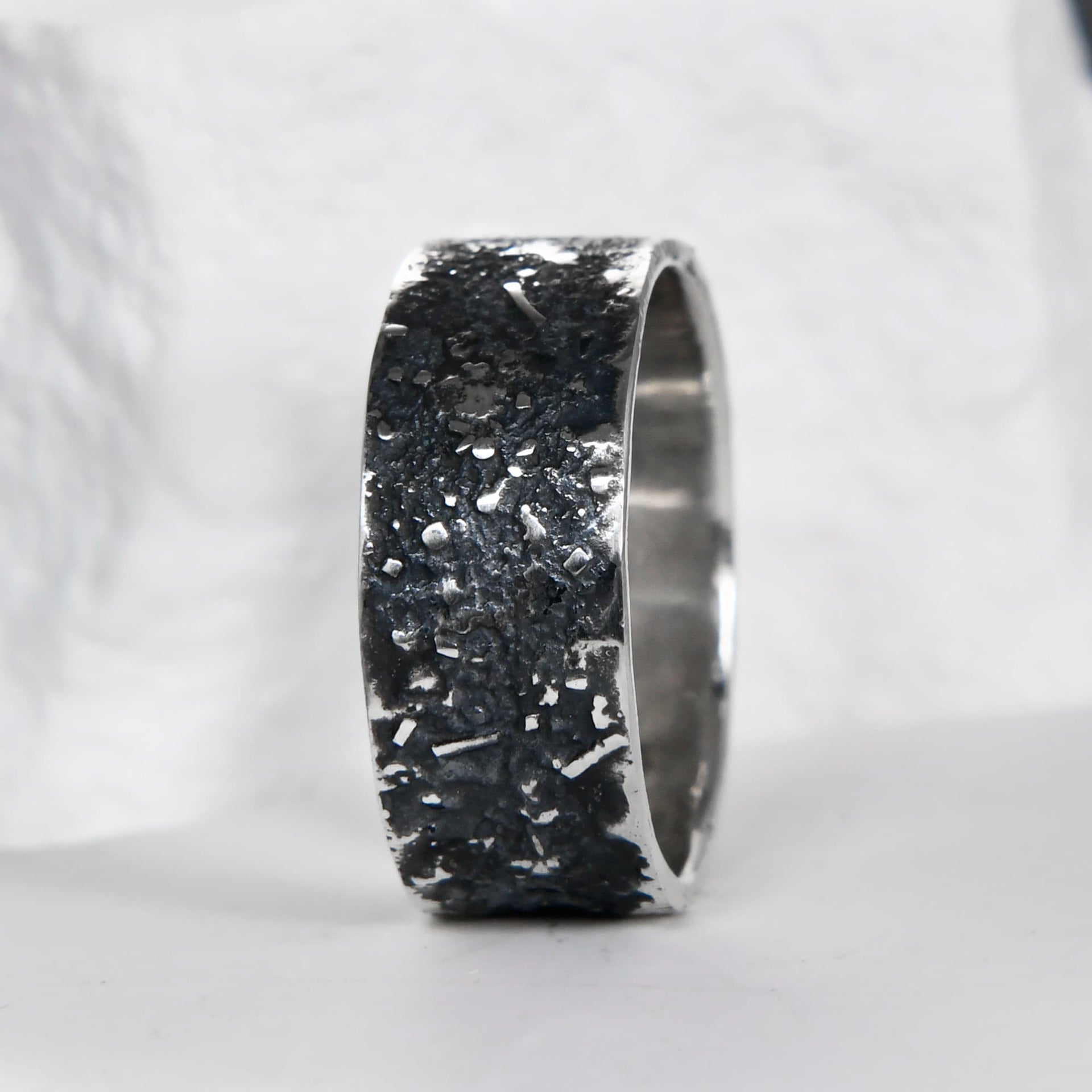 Silver galaxy ring shown from the side, with a rugged oxidized surface and polished edges.