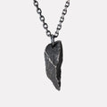 A dark, rugged silver pendant shaped like a sharp, angular rock with a rough, textured surface, hanging from a black oxidized chain against a plain white background.