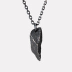A dark, rugged silver pendant shaped like a sharp, angular rock with a rough, textured surface, hanging from a black oxidized chain against a plain white background.