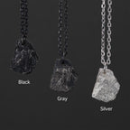 Three rugged silver pendants shaped like natural rocks, each hanging from a different chain. The finishes shown are Black with a dark chain, Gray with a muted chain, and Silver with a bright chain, displayed side by side on a dark background.