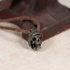Beanie skull pendant resting against a rusted red iron tool on cream felt, leather cord, gothic memento mori necklace