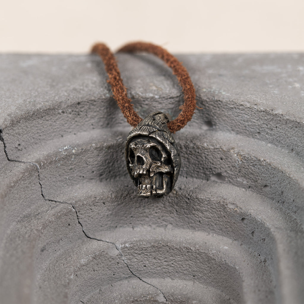 Beanie skull pendant on a cracked grey concrete arch, hand carved nickel silver hatted skull necklace