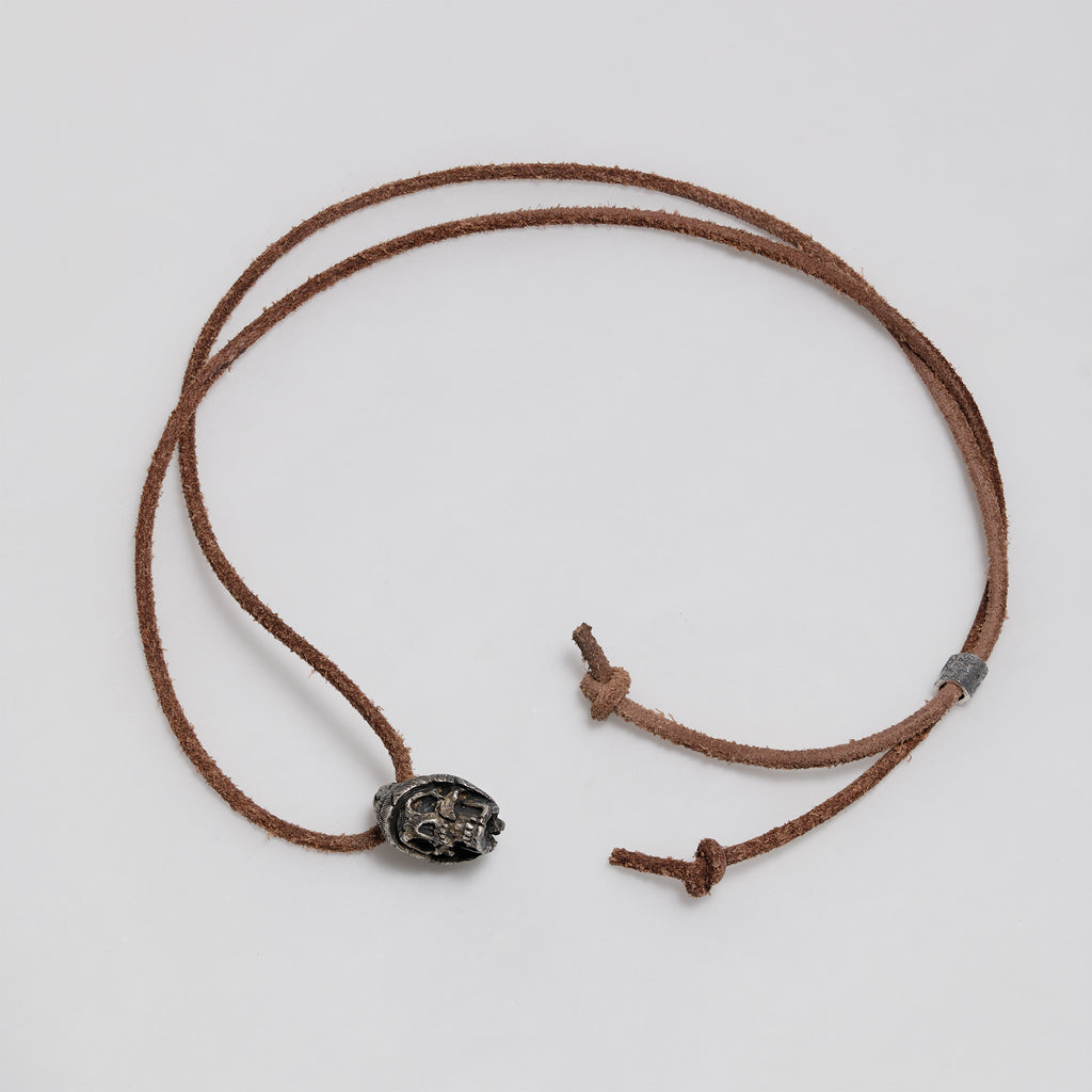 Full dark brown leather cord laid out in a loop with the beanie skull pendant, slider bead and knotted ends