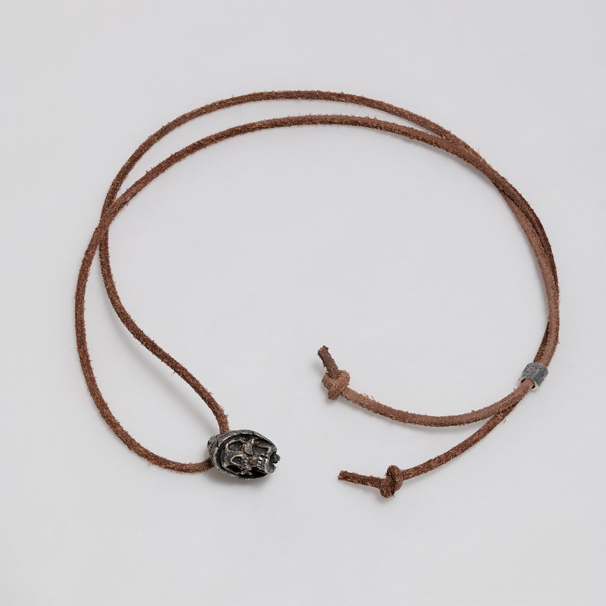 Full dark brown leather cord laid out in a loop with the beanie skull pendant, slider bead and knotted ends