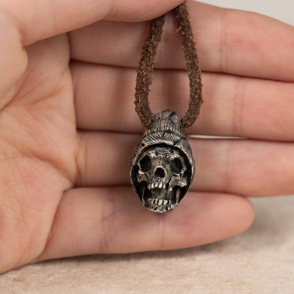 Beanie skull pendant held in an open palm on its leather cord, showing the pendant size in the hand