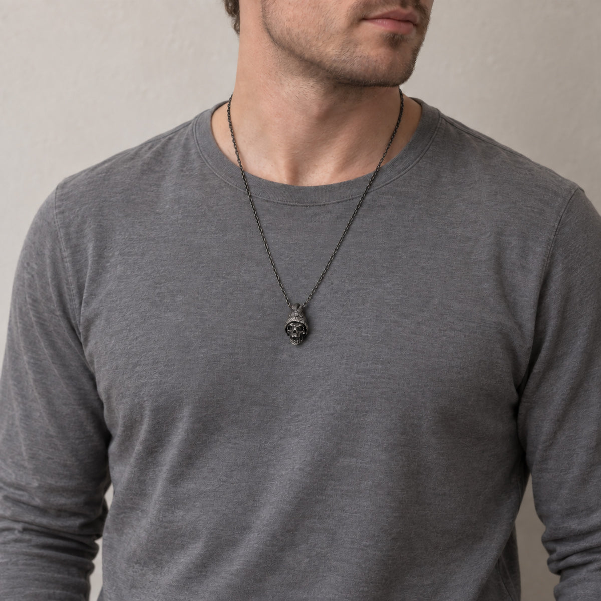 Man in a grey long-sleeve shirt wearing the beanie skull pendant on a dark chain at mid-chest