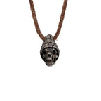 Men's beanie skull necklace in oxidized nickel silver, front view of the hand carved skull pendant in a ribbed knit beanie on a dark brown leather cord, white background