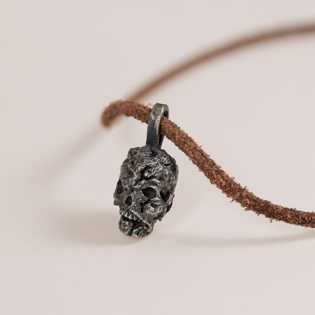 Side profile of the exposed brain skull pendant on a light surface, carved brain above the skull face, leather cord