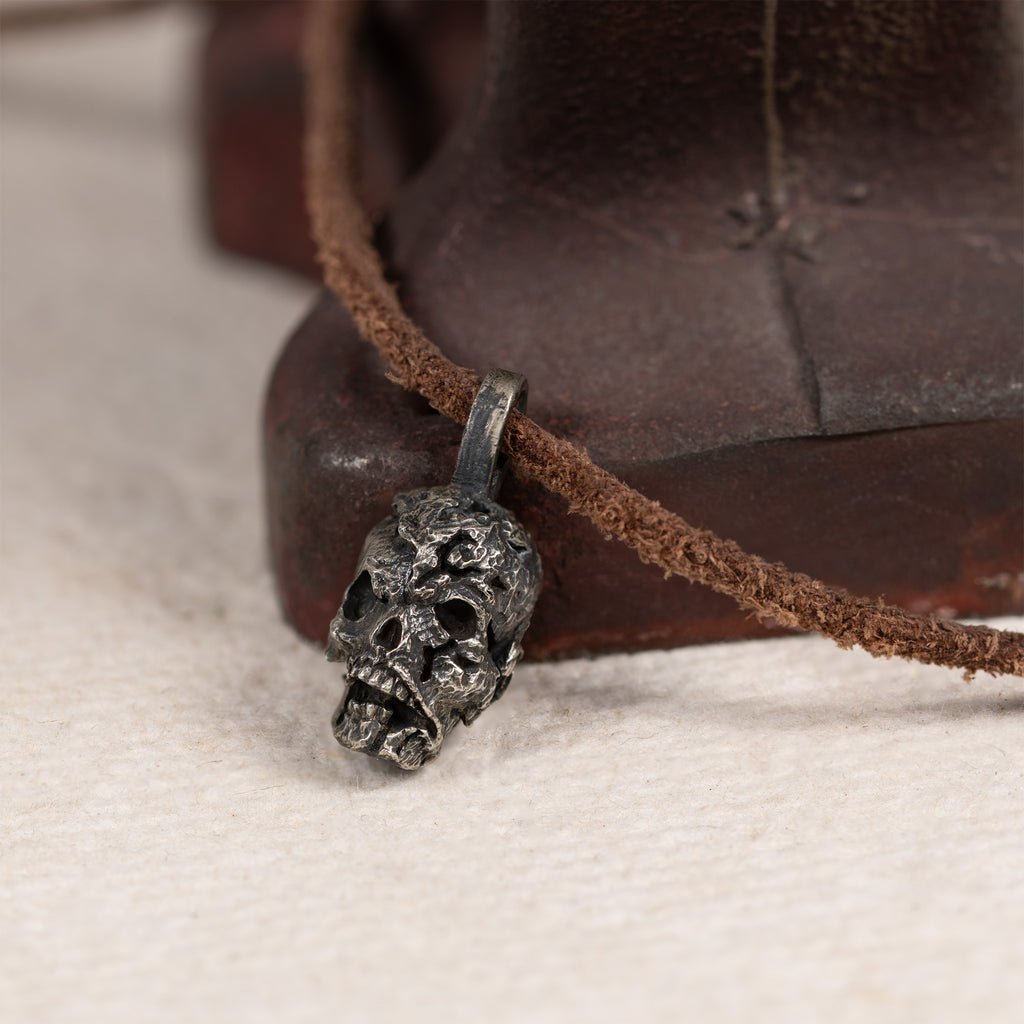 Exposed brain skull pendant resting against a rusted red iron tool on cream felt, leather cord, gothic anatomy necklace