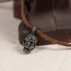 Exposed brain skull pendant resting against a rusted red iron tool on cream felt, leather cord, gothic anatomy necklace