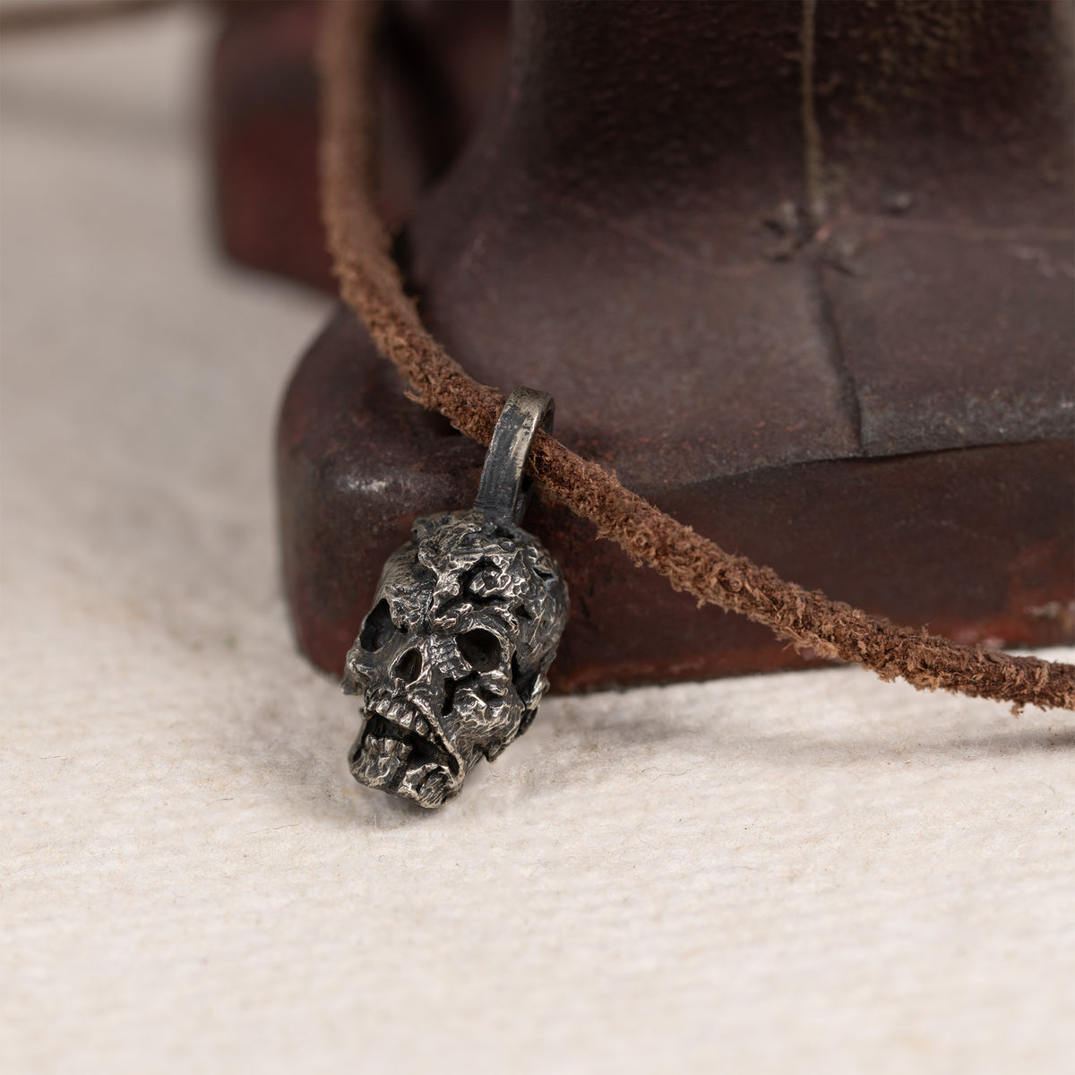 Exposed brain skull pendant resting against a rusted red iron tool on cream felt, leather cord, gothic anatomy necklace