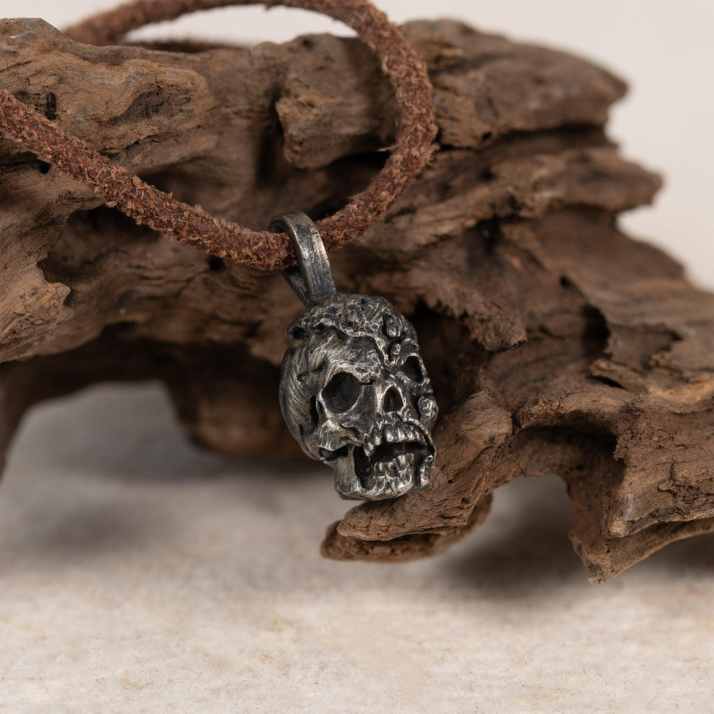 Exposed brain skull necklace hanging from a piece of driftwood, oxidized nickel silver pendant on a dark brown leather cord