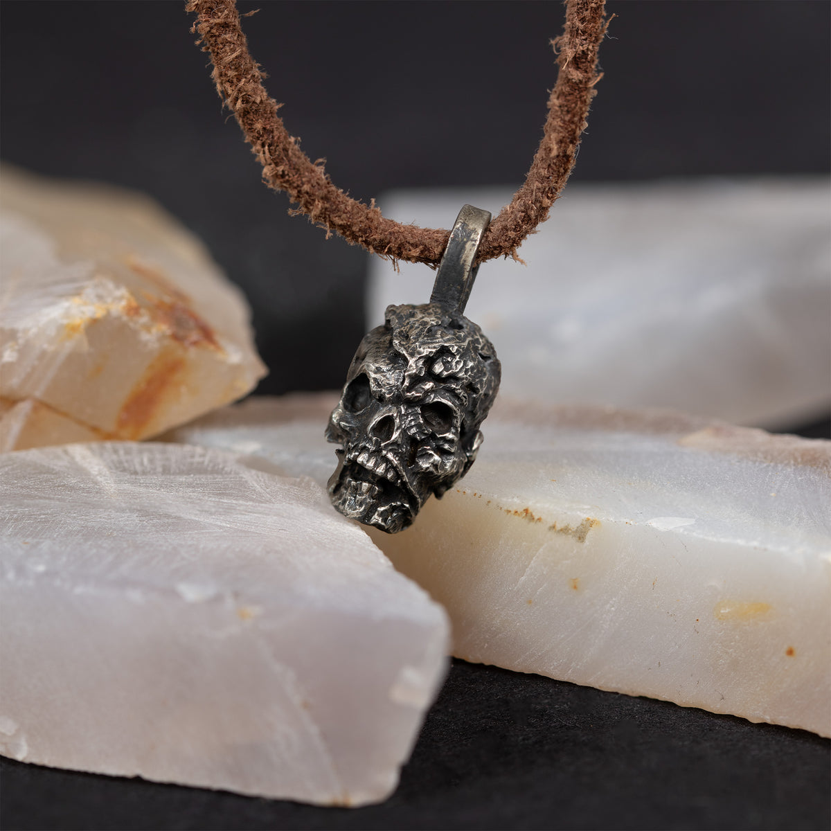 Exposed brain skull pendant on white quartz crystal against a dark background, hand carved nickel silver skull and brain necklace