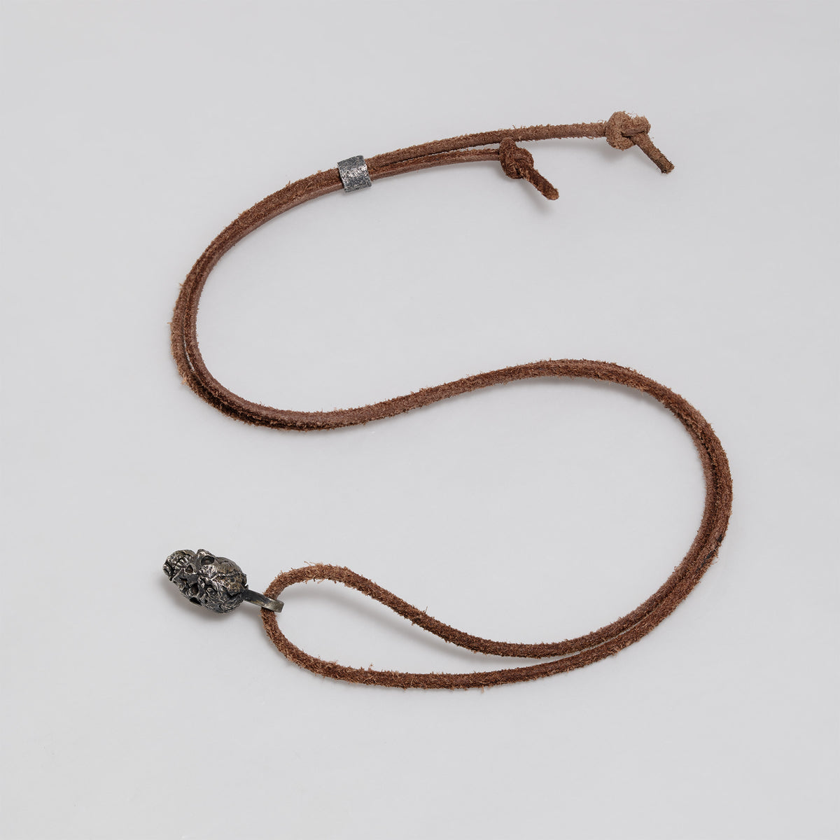 Full dark brown leather cord laid out in a loop with the exposed brain skull pendant, slider bead and knotted ends