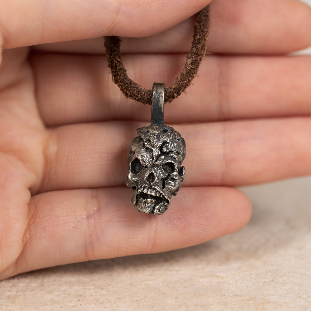 Exposed brain skull pendant held in an open palm on its leather cord, showing the pendant size in the hand