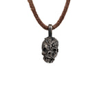 Men's exposed brain skull necklace in oxidized nickel silver, front view of the hand carved skull pendant with an open cranium on a dark brown leather cord, white background
