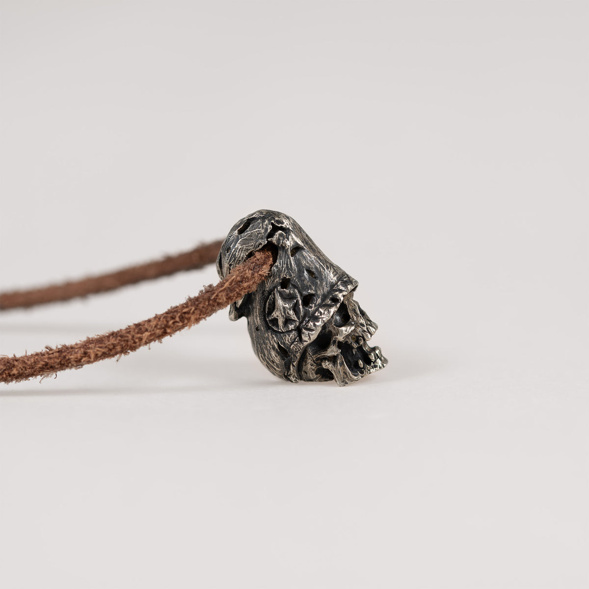Side profile of the top hat skull pendant lying on a light grey surface, carved hat brim over the skull face, leather cord