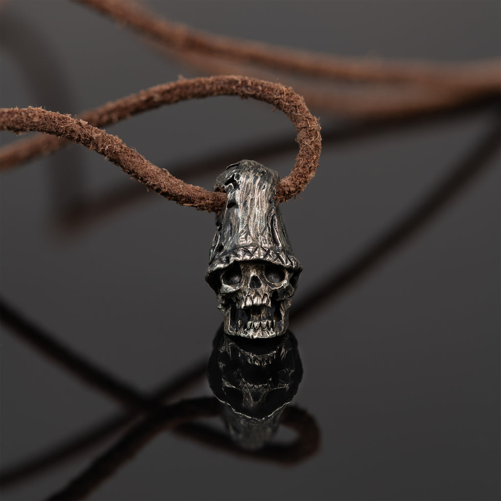 Top hat skull necklace standing on dark reflective glass with its mirror image, oxidized nickel silver skull pendant on a leather cord
