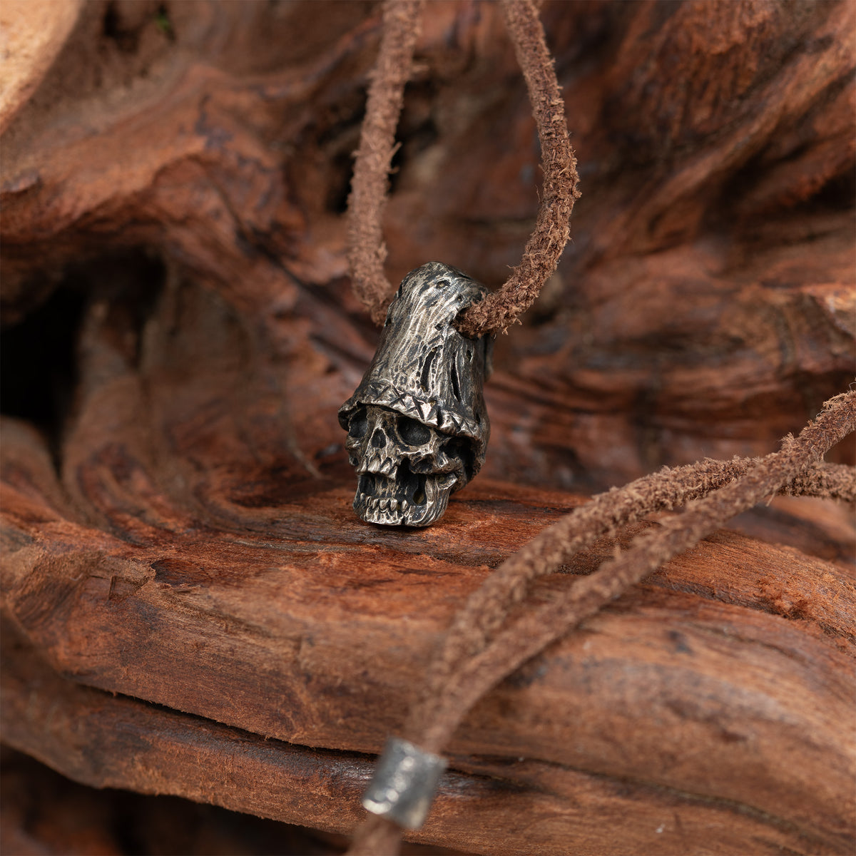 Top hat skull necklace hanging from a piece of driftwood, oxidized nickel silver pendant on a dark brown leather cord