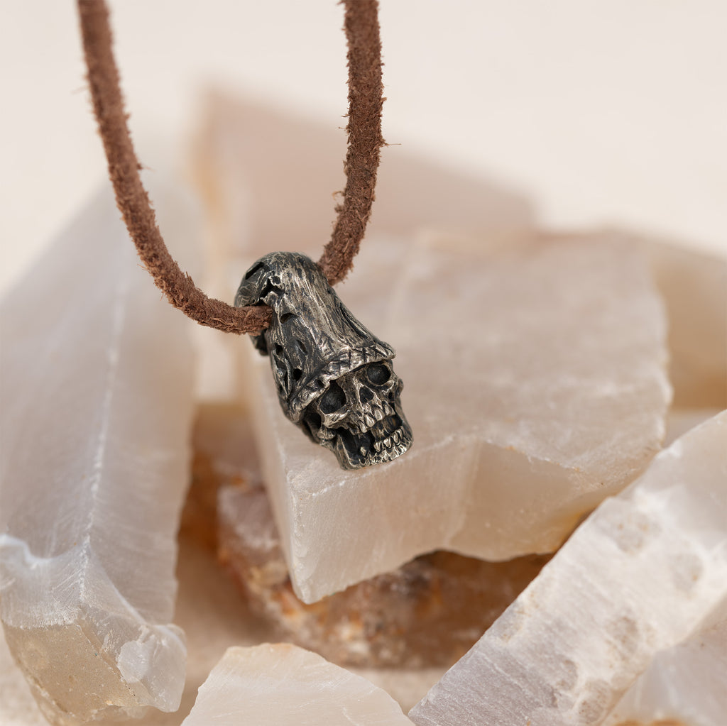 Top hat skull pendant on white quartz crystal against a dark background, hand carved nickel silver skull necklace