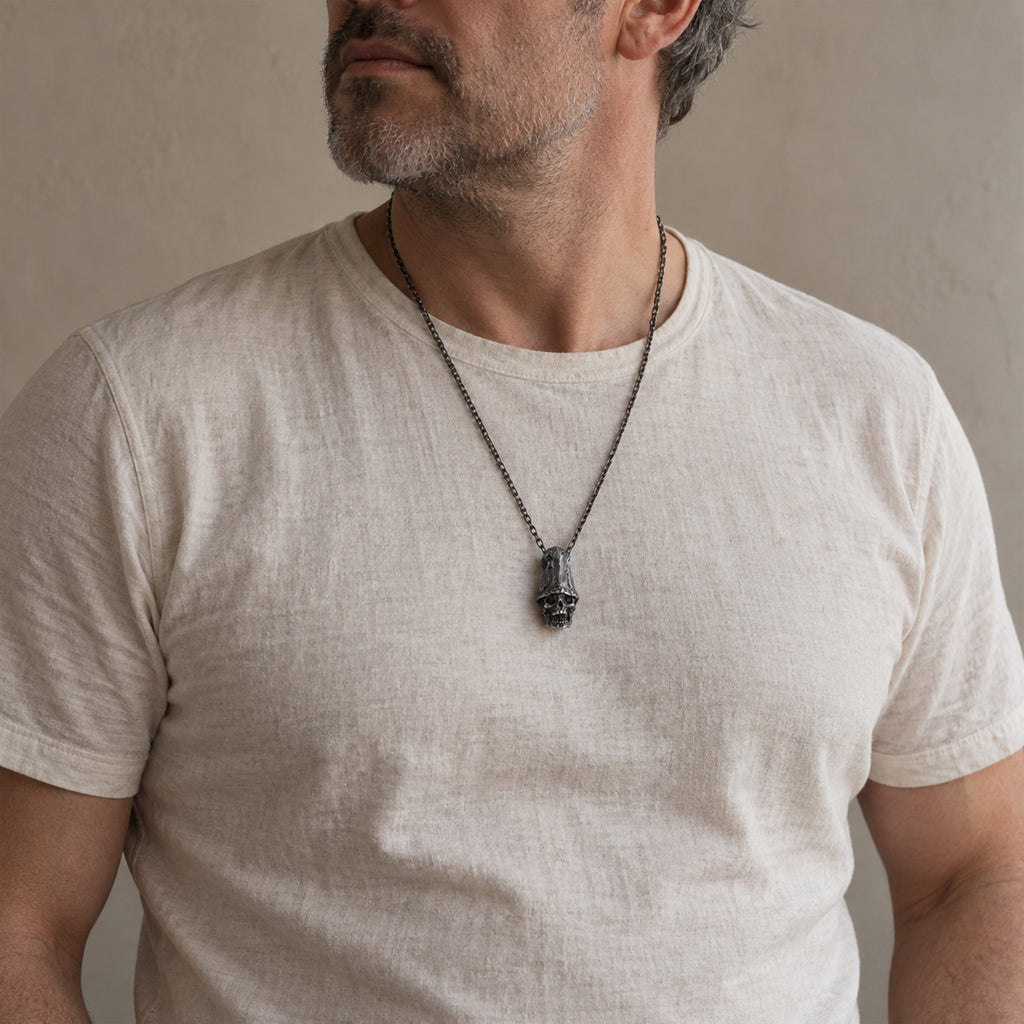 Man in a grey long-sleeve shirt wearing the top hat skull pendant on a dark chain at mid-chest