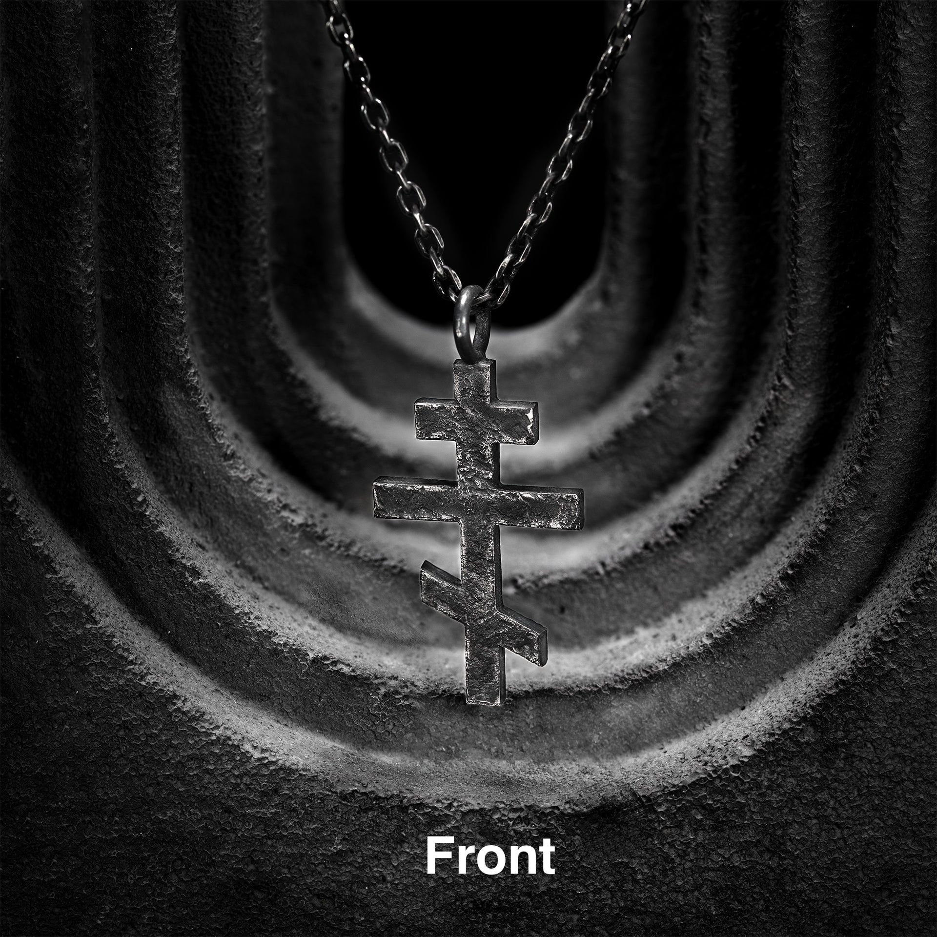Close-up detail of the weathered hand-carved texture on a black sterling silver Orthodox cross necklace