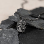Oxidized 925 sterling-silver skull pendant on natural slate, showing the black-gray finish and carving depth.