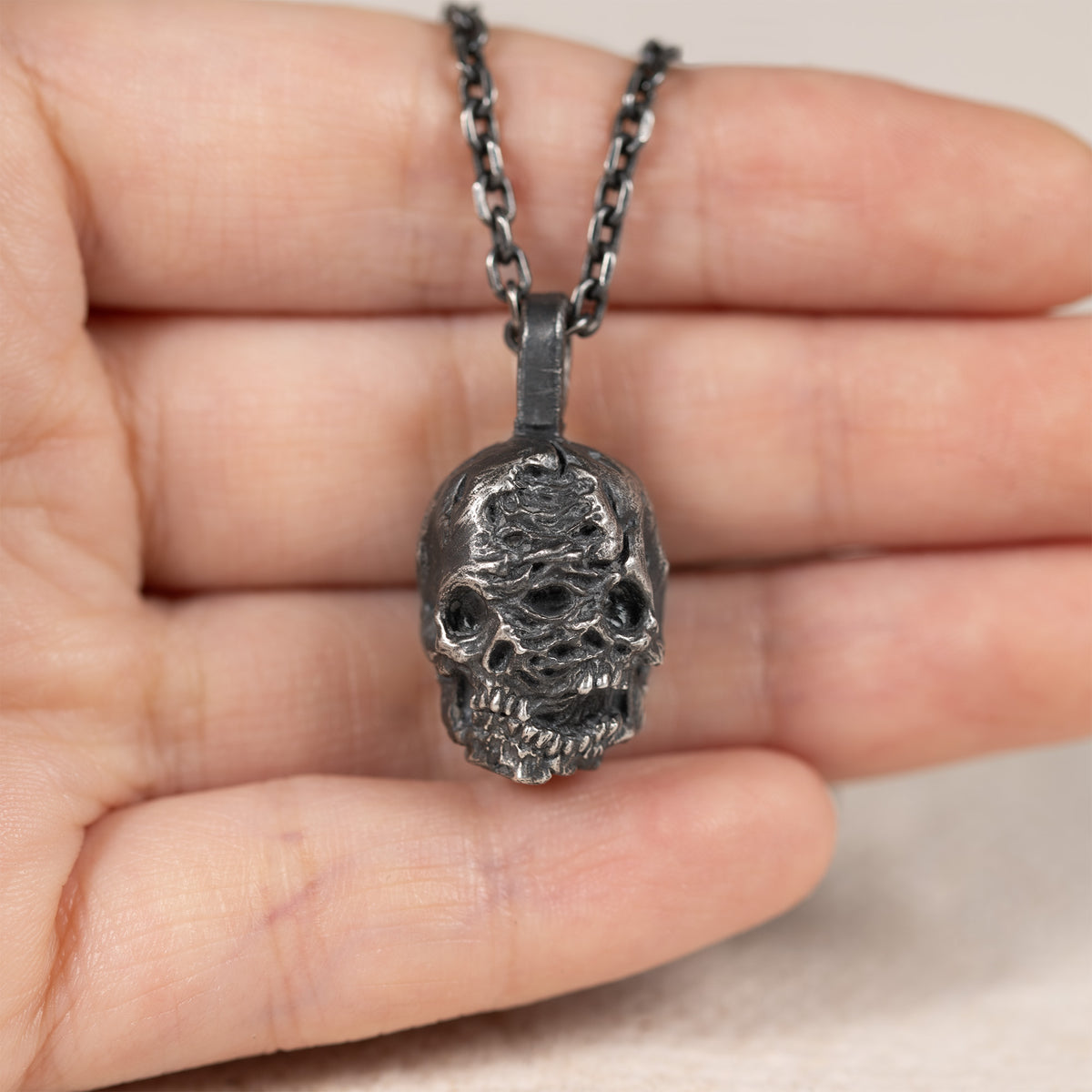Double-face skull pendant held in a hand to show its real-world size.