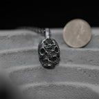 Double-face skull pendant beside a coin for a size comparison in millimeters.